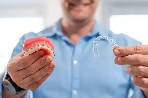 Orthodontist holding a dental model with braces and a clear aligner to explain adult orthodontic treatment age limit