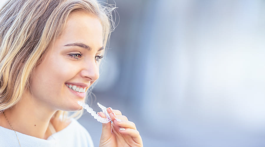 A smiling woman holding a clear dental aligner near her face